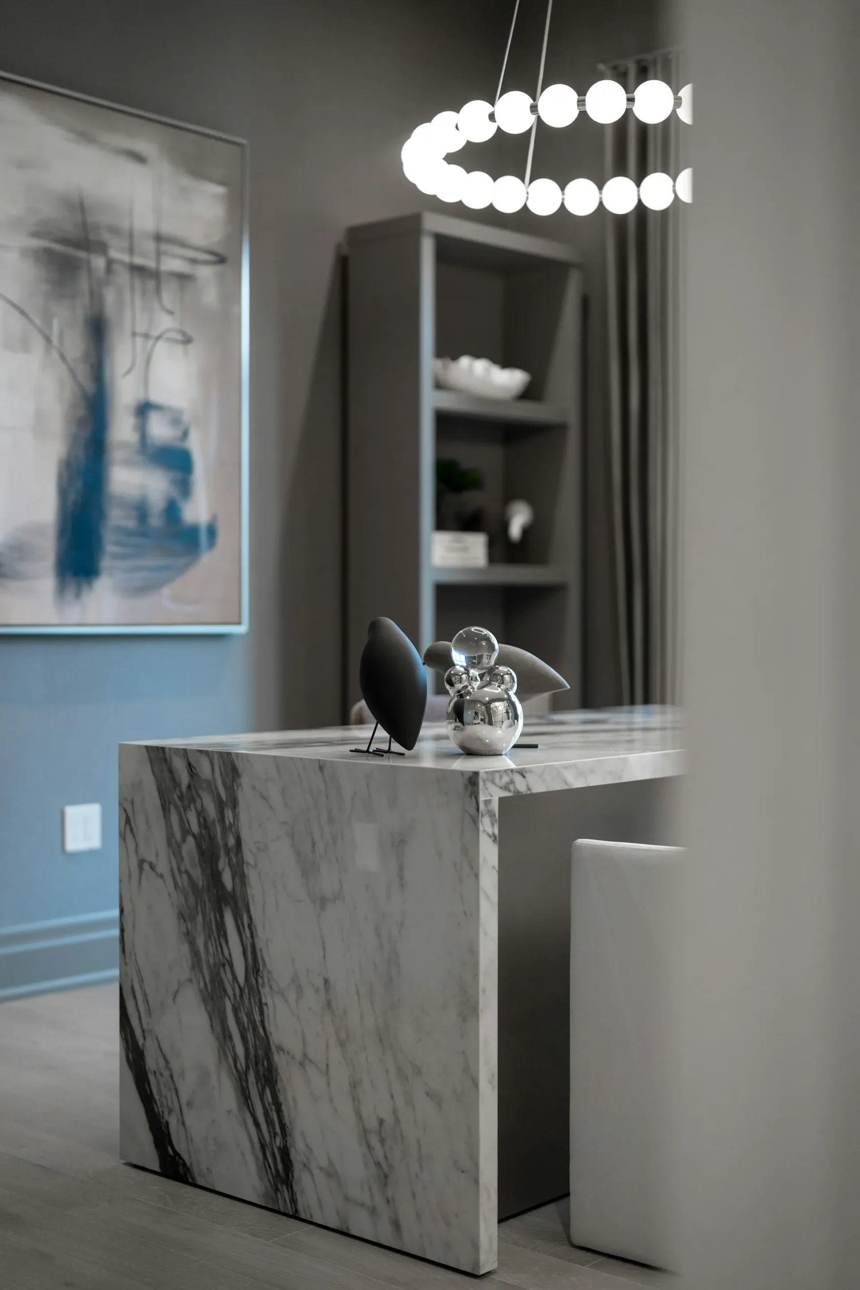 Modern dining room with marble table, wall art, and hanging light.